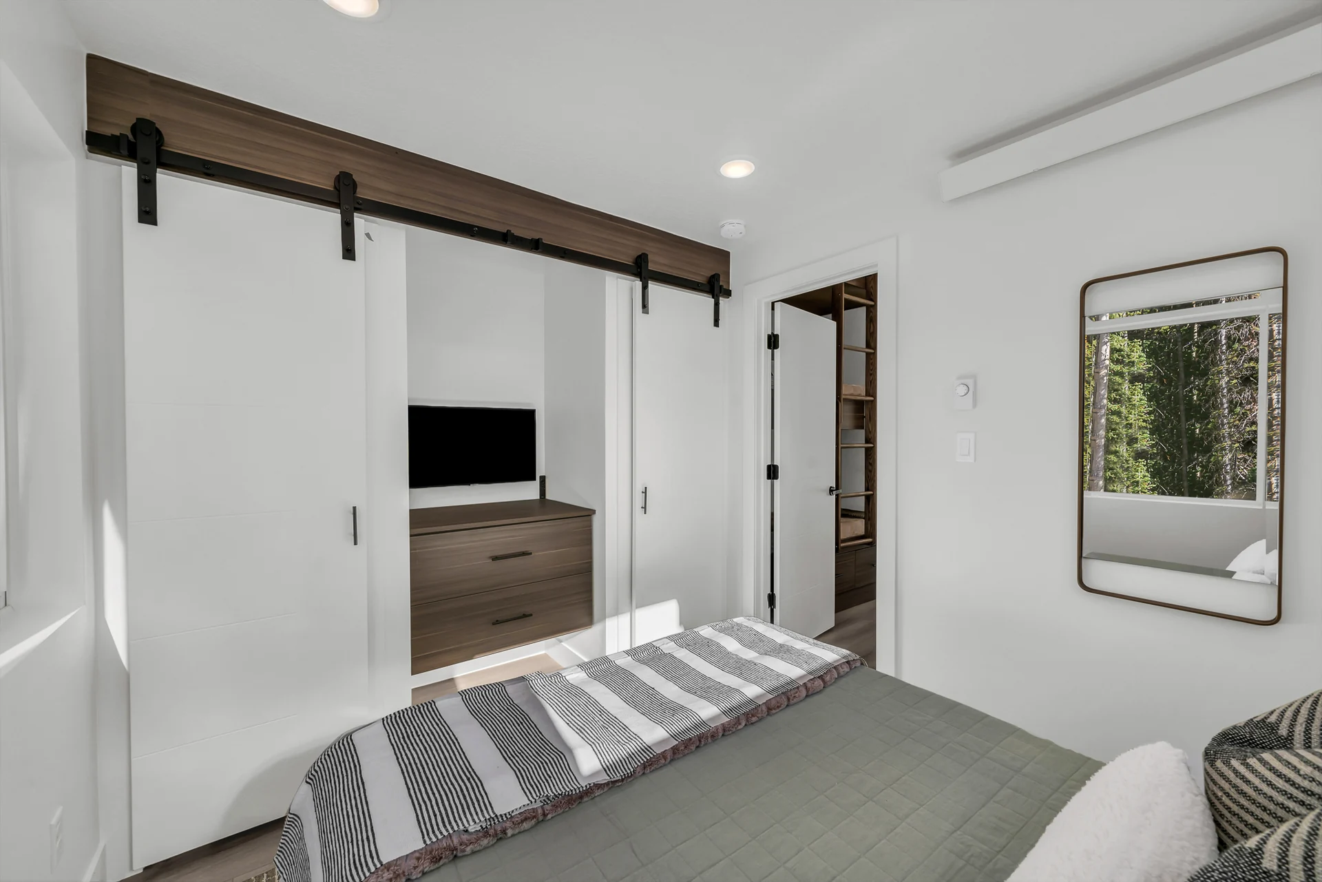 Reverse bedroom view with part of the bed, a black TV between sliding closet doors, a mirror, dresser and doorway toward the main living space.