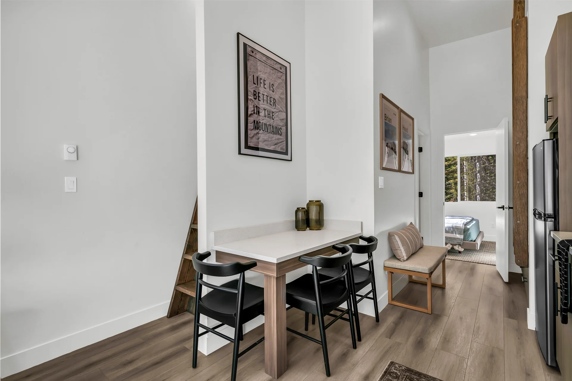 Compact table with four black chairs beside the kitchen; steep wooden loft steps to the left and the downstairs bedroom doorway behind.