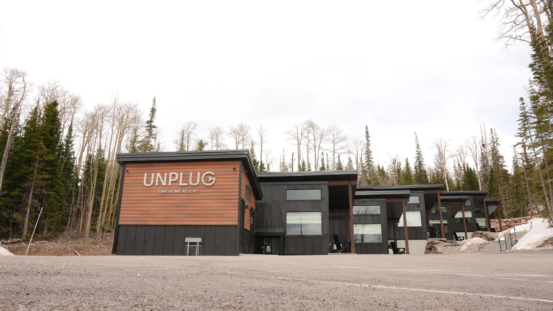 Unplug sign and cabin row behind paved frontage, with stone retaining walls, gravel beside the steps and real seasonal snowbanks.