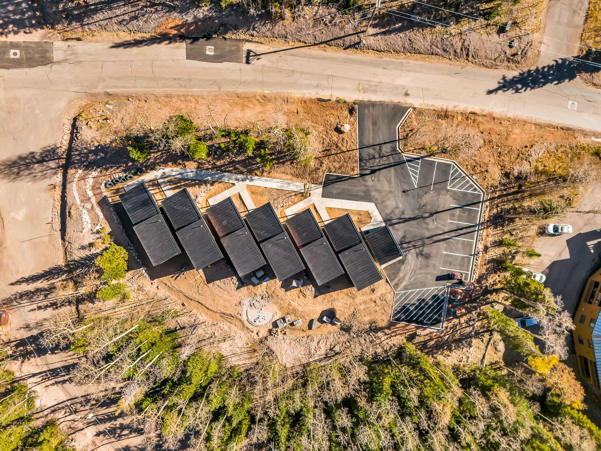 Overhead view of the cabin roofs, paths, road, striped parking area and circular fire-pit space behind the cabins.
